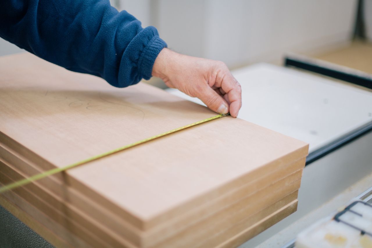 About Close-up of a carpenter's hand using a tape measure to measure wooden planks indoors.